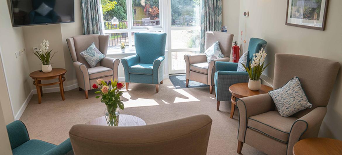 A contemporary mix of teal and beige large arm chairs located around the outer edges of the seating area towards a wall mounted television and access to the garden area.